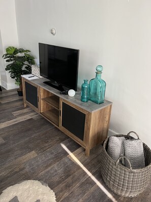Un moble d'entreteniment de fusta amb un televisor de pantalla plana, dues ampolles de vidre i un comandament a distància.