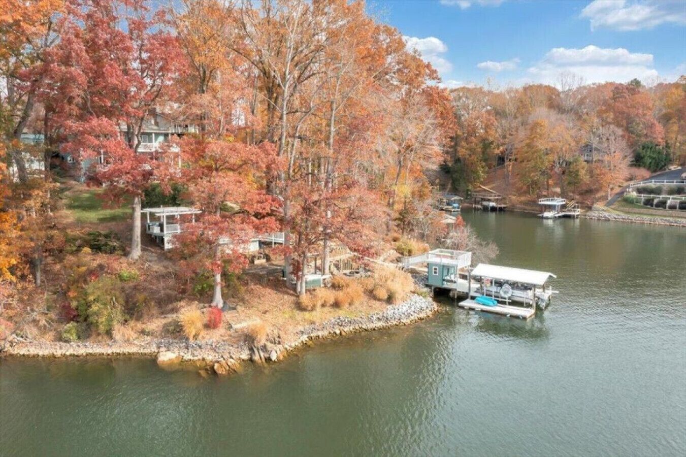 A lakeside property with a dock and boats, surrounded by autumn-colored trees.