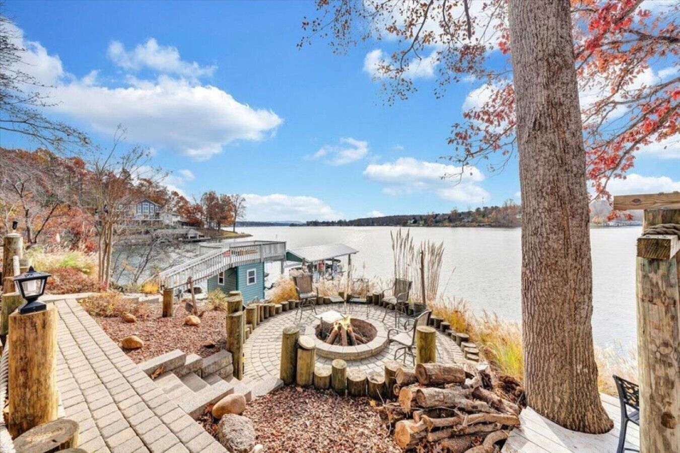 Une terrasse au bord du lac, avec un foyer, des bancs en bois et une vue sur le lac et les bâtiments situés au loin.