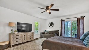Een slaapkamer met een bed, een televisie, een plafondventilator, een dressoir en een raam met gordijnen.