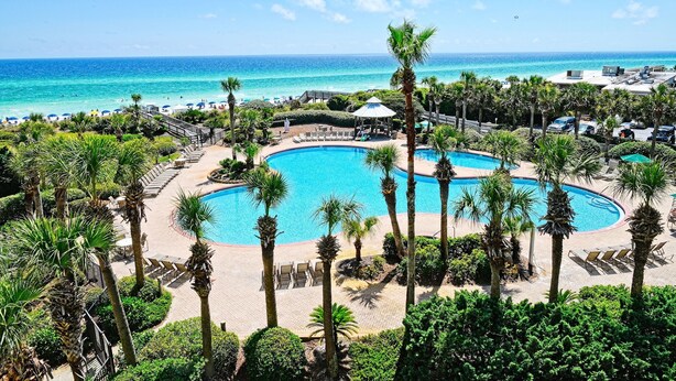 Ein Resort mit einem großen Pool, umgeben von Palmen und Liegestühlen, mit Blick auf einen Strand und das Meer.
