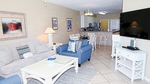 Ein Wohnzimmer mit Sofa, Couchtisch und TV-Schrank. Im Hintergrund ist eine Küchenzeile erkennbar.