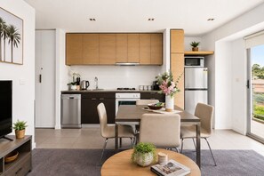 Uma cozinha moderna com armários de madeira, uma sala de jantar com mesa e cadeiras, e vista para o exterior por uma porta deslizante.