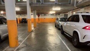 Ett parkeringshus med flera våningar, betongpelare, markerade parkeringsplatser och parkerade fordon.