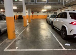 Un estacionamiento de varios niveles con pilares de hormigón, espacios delimitados y vehículos estacionados.