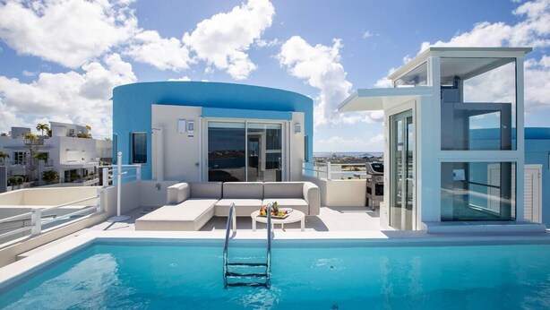 A modern pool area with a clear view of the sea, a lounge with a sofa, and a glass-enclosed structure. - Serenity Penthouse - The Pinnacle of Luxury (Maho)