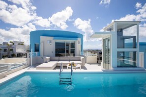 Een modern zwembadgedeelte met vrij uitzicht op zee, een lounge met een bank en een glazen structuur.