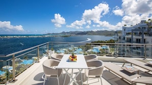 A balcony with a white table and chairs, overlooking a coastal view with mountains and a clear sky. - Serenity Penthouse - The Pinnacle of Luxury (Maho)