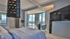 A modern hotel room with a large bed, a TV, and a balcony with a view of the sea. - Serenity Penthouse - The Pinnacle of Luxury (Maho)