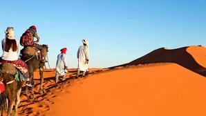A group of people riding camels across a desert landscape with sand dunes.