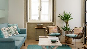 A living room with a sofa, two wicker chairs, a coffee table, and a potted plant.