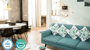 A modern living room with a teal sofa, a dining area with a round table, and a kitchen in the background.