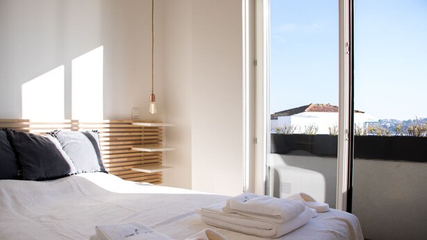 A modern bedroom with a large bed, neatly folded towels, and a view of a building through a large window.