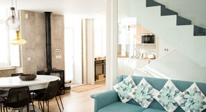 A modern living room with a teal sofa, a dining area with a round table, and a kitchen in the background.