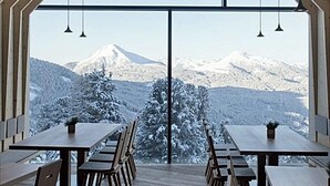 Een eetruimte met uitzicht op besneeuwde bergen door grote ramen.
