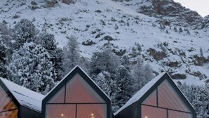 Drie moderne, glazen dakbedekte hutten met houten inrichting, gelegen voor een besneeuwde berg.