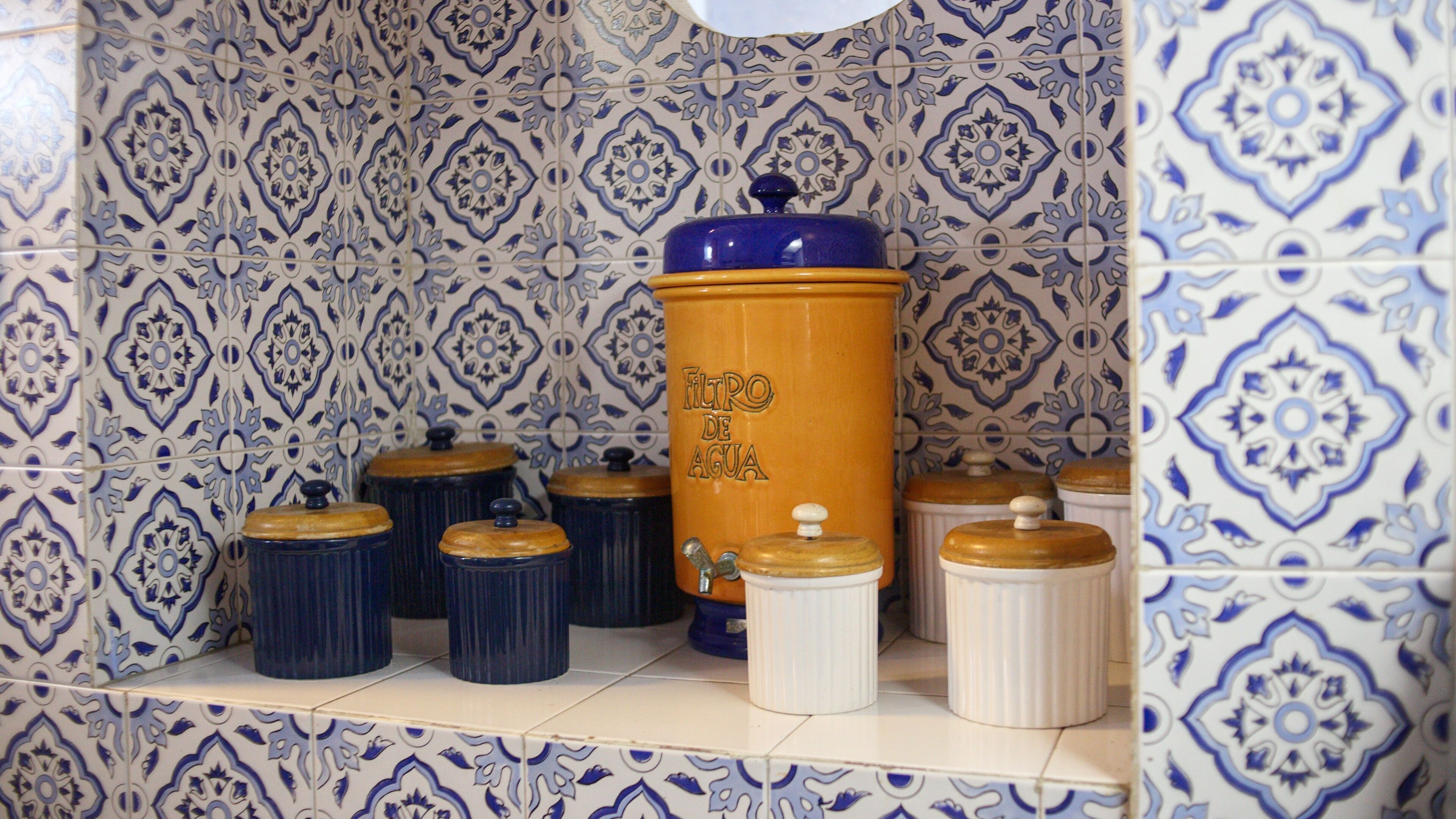 A kitchen shelf with various ceramic containers, including a tall orange container labeled "FILTRO DE AGUA" and several smaller blue and white containers.