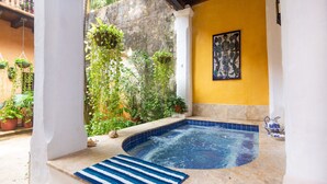 A hot tub area with a stone floor, surrounded by potted plants and a yellow wall. - Casa Baloco (Cartagena)
