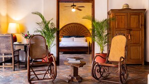 A room with a bed, two rocking chairs, a small table with books, a lamp, and a ceiling fan. - Casa Baloco (Cartagena)