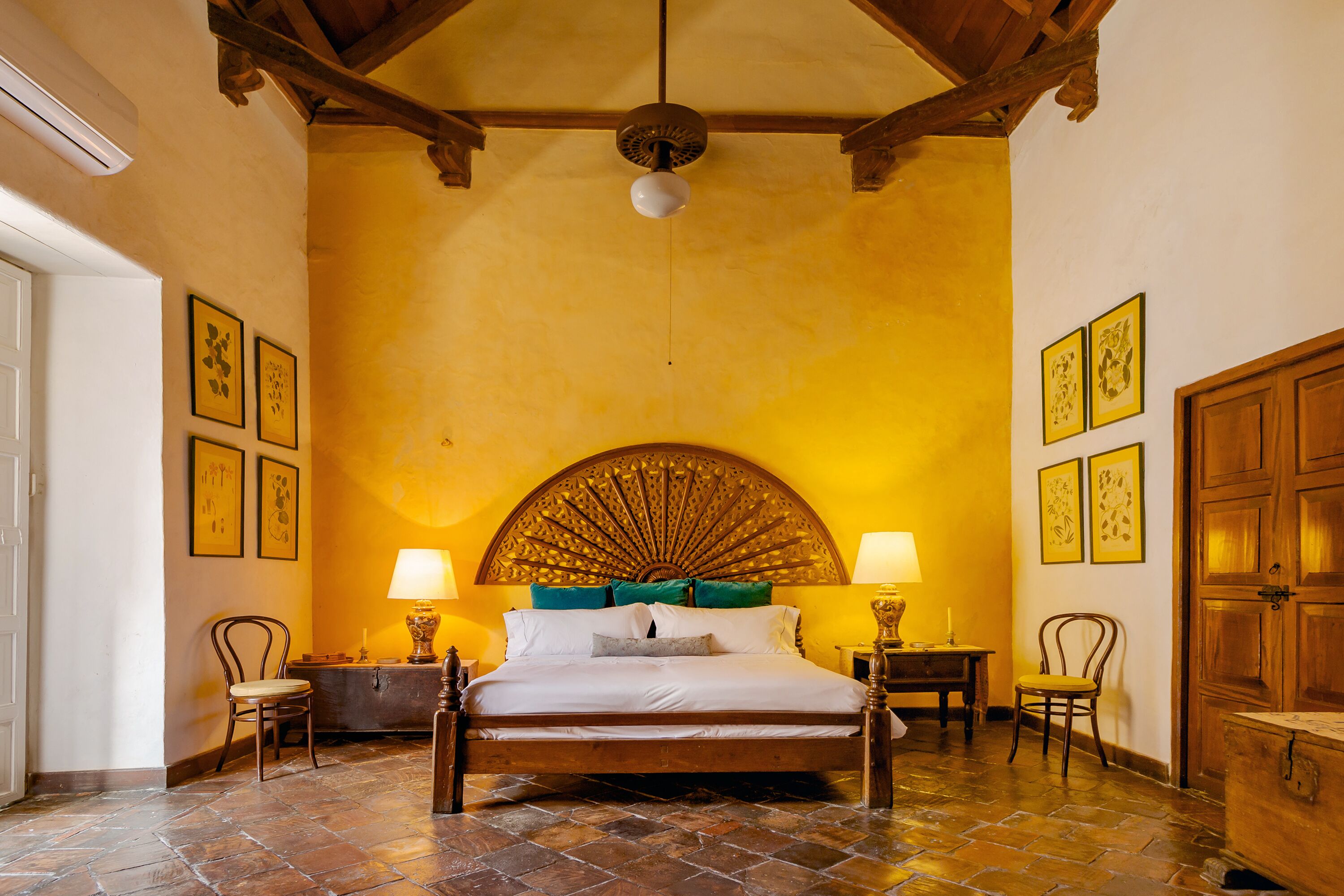 A room with a large bed, wooden headboard, two chairs, a table, and a wooden wardrobe.