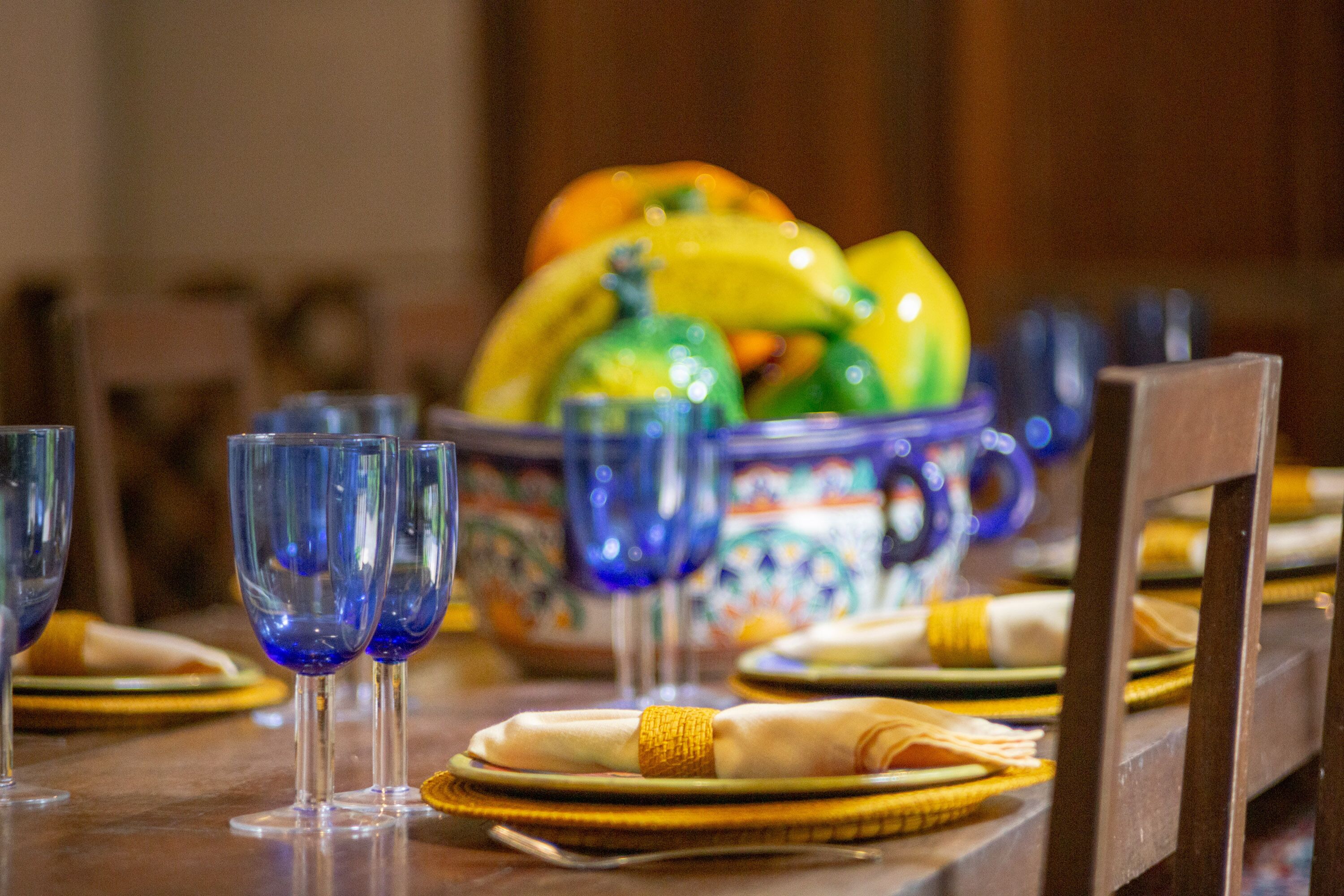 A dining table with blue glassware, plates, and a bowl of fruit.