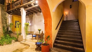 A staircase leading to an upper level, with a balcony above. There are potted plants and a table with chairs outside. - Casa Baloco (Cartagena)