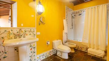 Un bany amb una paret groga, un lavabo, dues vàteres, una dutxa i un mirall.