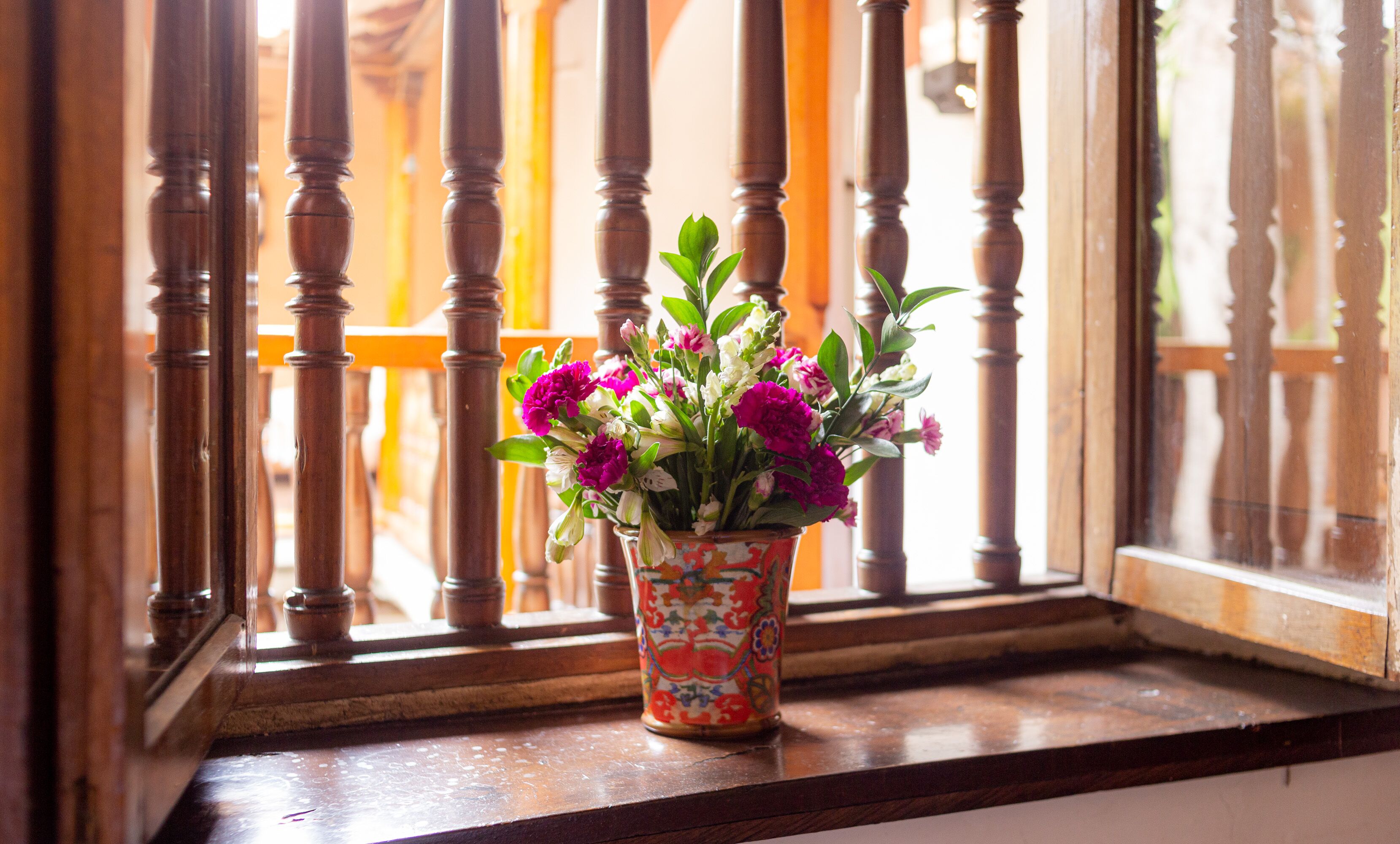 Una ventana con barandilla de madera y un florero con flores sobre un alféizar de madera.