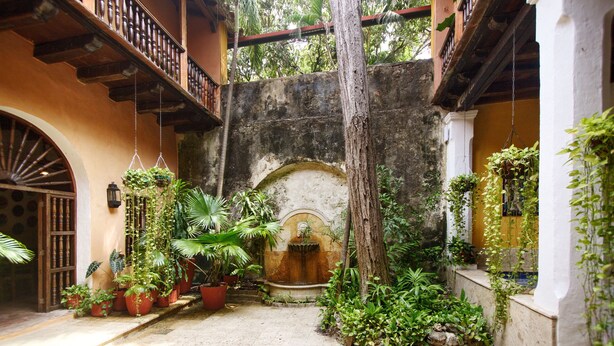 A courtyard with potted plants, a stone fountain, and a wooden balcony. - Casa Baloco (Cartagena)
