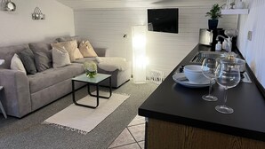 Una sala de estar moderna con un sofá, una mesa de centro y una zona de cocina con mostrador, copas de vino y un televisor.