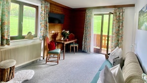 A room with a dining table, chairs, a sofa, a radiator, and a TV mounted on the wall.