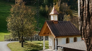A small church with a bell tower, surrounded by a stone wall and a paved path.