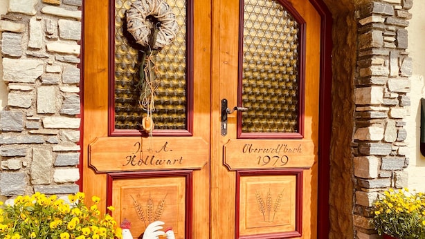 A wooden double door with glass panels, a stone wall, and a red mat at the entrance.