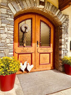 Uma porta dupla de madeira com painéis de vidro, uma parede de pedra e um tapete vermelho na entrada.