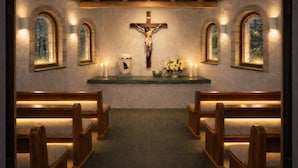 A church interior with wooden pews, a crucifix, candles, and a floral arrangement.