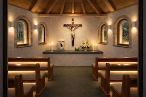 Interno di una chiesa con panche di legno, una crocifissa, candele e un'esposizione floreale su un tavolo.