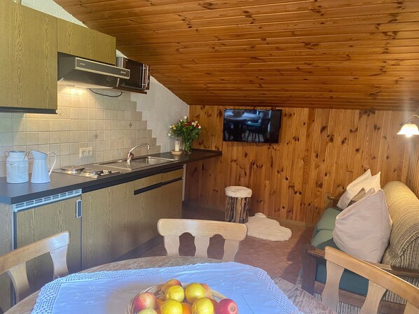 A kitchen with a wooden ceiling, a TV mounted on the wall, and a dining area with a table set for two.