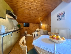 Eine gemütliche Küche mit Holzwänden, einem Esstisch mit Obstkorb und einem an der Wand montierten Fernseher.