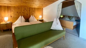 Une pièce avec un plafond en bois, un canapé-lit vert, un petit tabouret et une table de chevet avec une lampe.