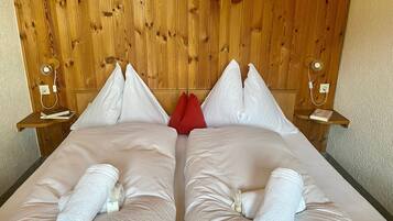 A double bed with white linens and pillows, wooden headboard, bedside tables with lamps, and a red accent pillow.
