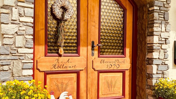 Une porte à deux battants en bois, avec des panneaux de verre, un mur en pierre et un paillasson rouge à l’entrée.