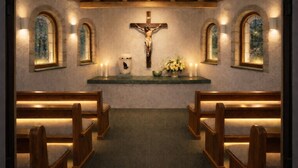 L’intérieur d’une église avec des bancs en bois, un crucifix, des bougies et un arrangement floral.