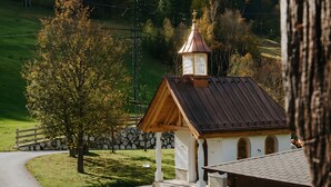 Une petite église dotée d’un clocher, entourée d’un mur de pierre et bordée d’un chemin pavé.