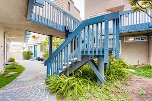 Stairs lead to a contemporary building with a geometric design, surrounded by lush greenery and a paved pathway.