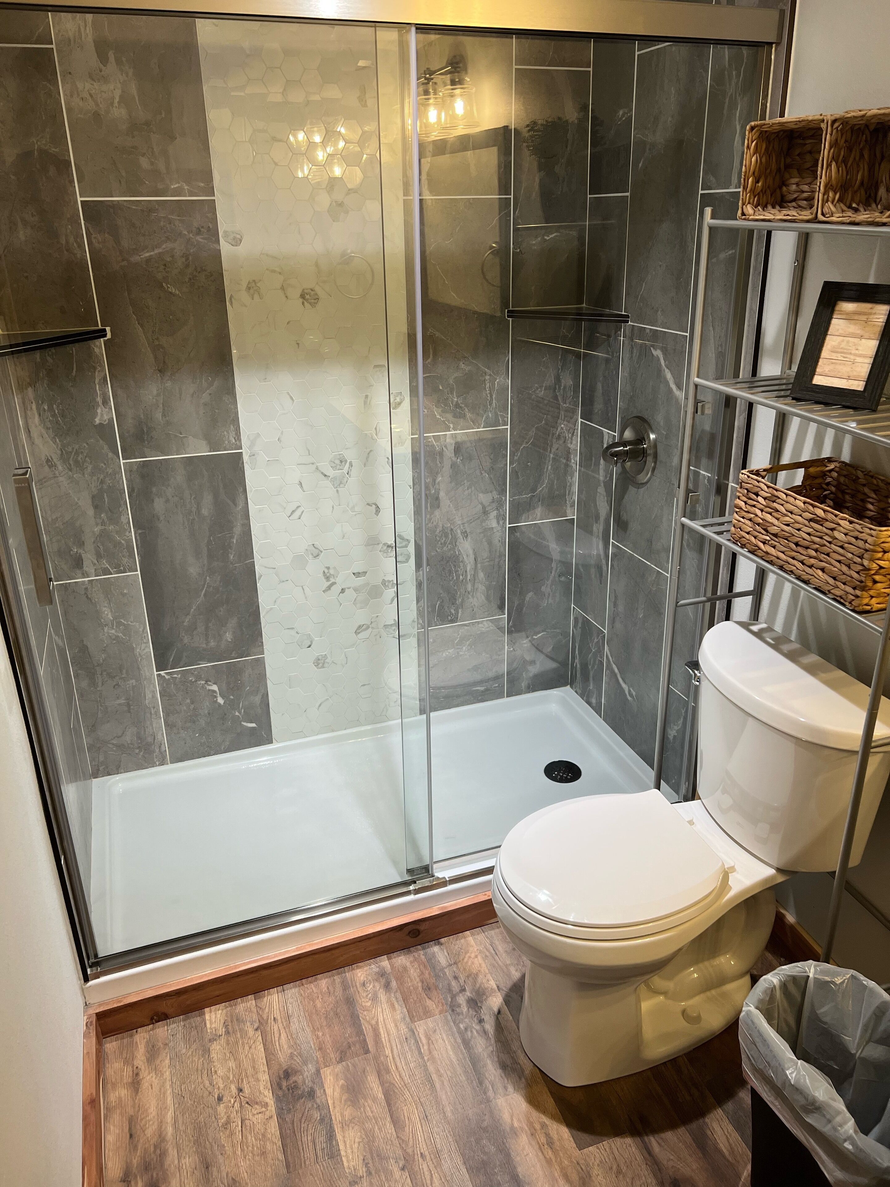 A modern bathroom with a glass-enclosed shower, a toilet, and a wooden floor.