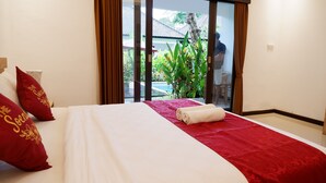 A hotel room with a bed, red and white bedding, a red throw, and a view of a pool and greenery outside.