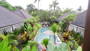 A pool surrounded by lush greenery and white buildings with tiled roofs.