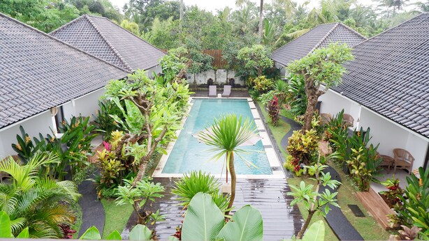 A pool surrounded by lush greenery and white buildings with tiled roofs.