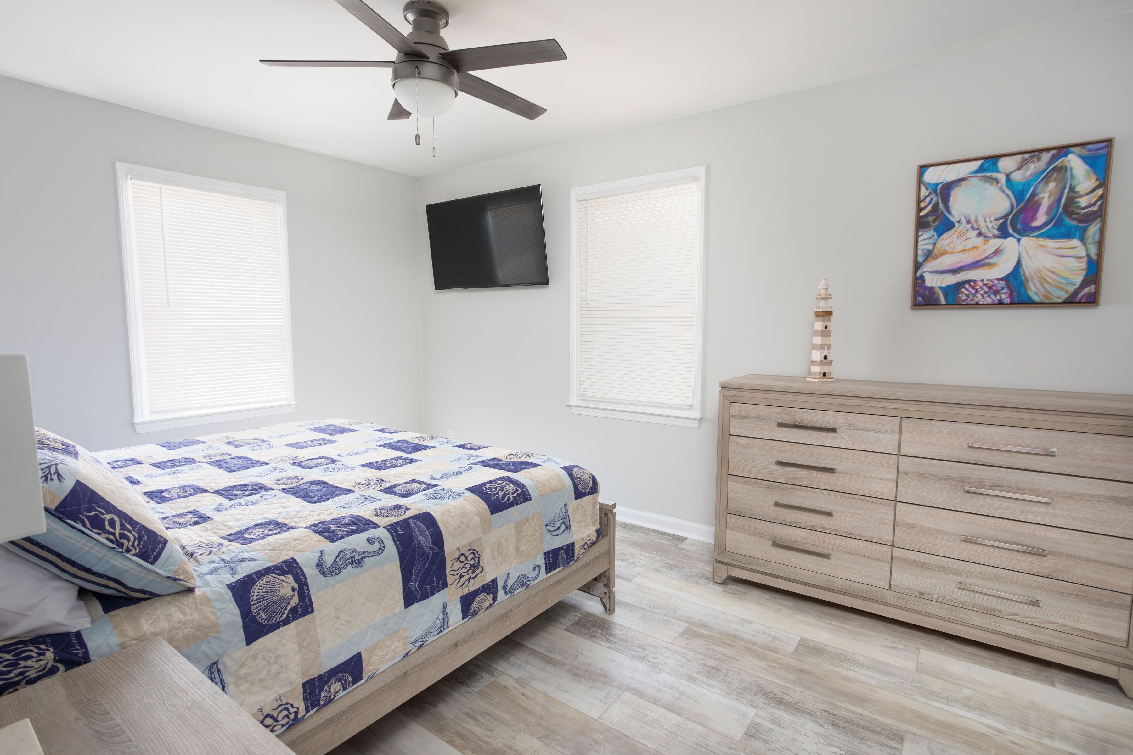 Un dormitorio con cama, cómoda, ventilador de techo, televisor y un cuadro.