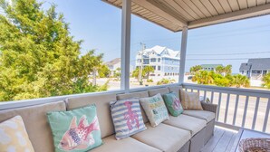 A covered outdoor seating area with a sofa and cushions, overlooking a residential street and buildings. - Pool Paradise: 8 bedroom 6 bath private pool sleeps 20 across from the beach! (Murrells Inlet)